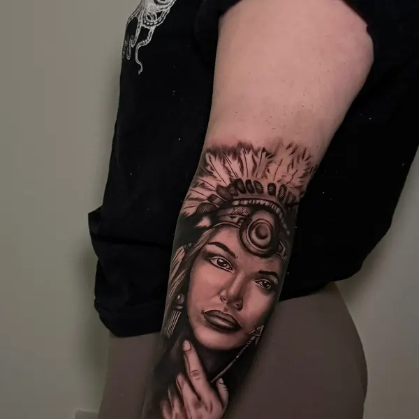 black and grey realism portrait of a woman in a feathered headdress, forearm piece, by cameron at shade studio peterborough
